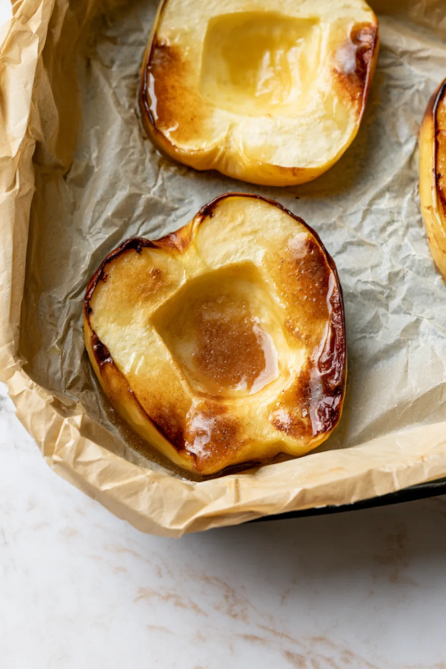 Cored apple halves roasted in an air fryer basket on parchment, with butter and brown sugar melted in the cavities