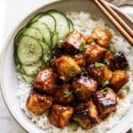 Honey garlic salmon bowl with glazed salmon cubes over white rice, sesame cucumber salad, sliced green onion and chopsticks on the rim